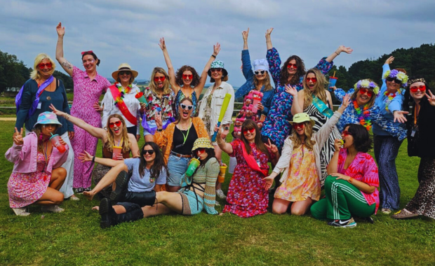 Group of hens in colourful costumes at HenFest™, highlighting the Maid of Honour’s role in planning.