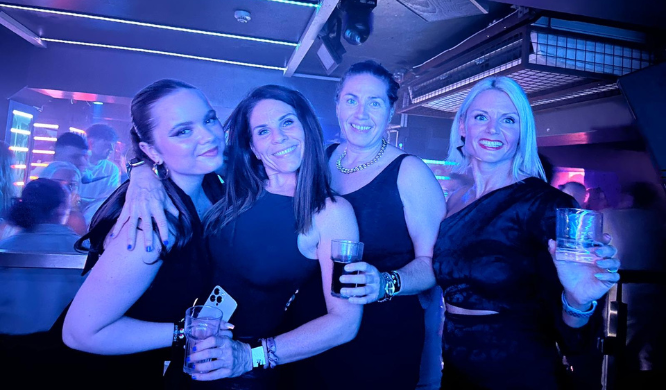 Friends celebrating Galentine’s Day on a night out, smiling and holding drinks under club lights